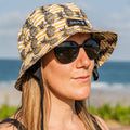 Woman wearing a Amity Blue patterned pineapple surf bucket hat and sunglasses on a beach