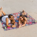 Two people lying on a colorful beach blanket on a sandy surface