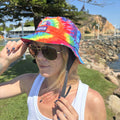 Person wearing a colorful tie-dye bucket hat and sunglasses outdoors. Amity blue logo on hat