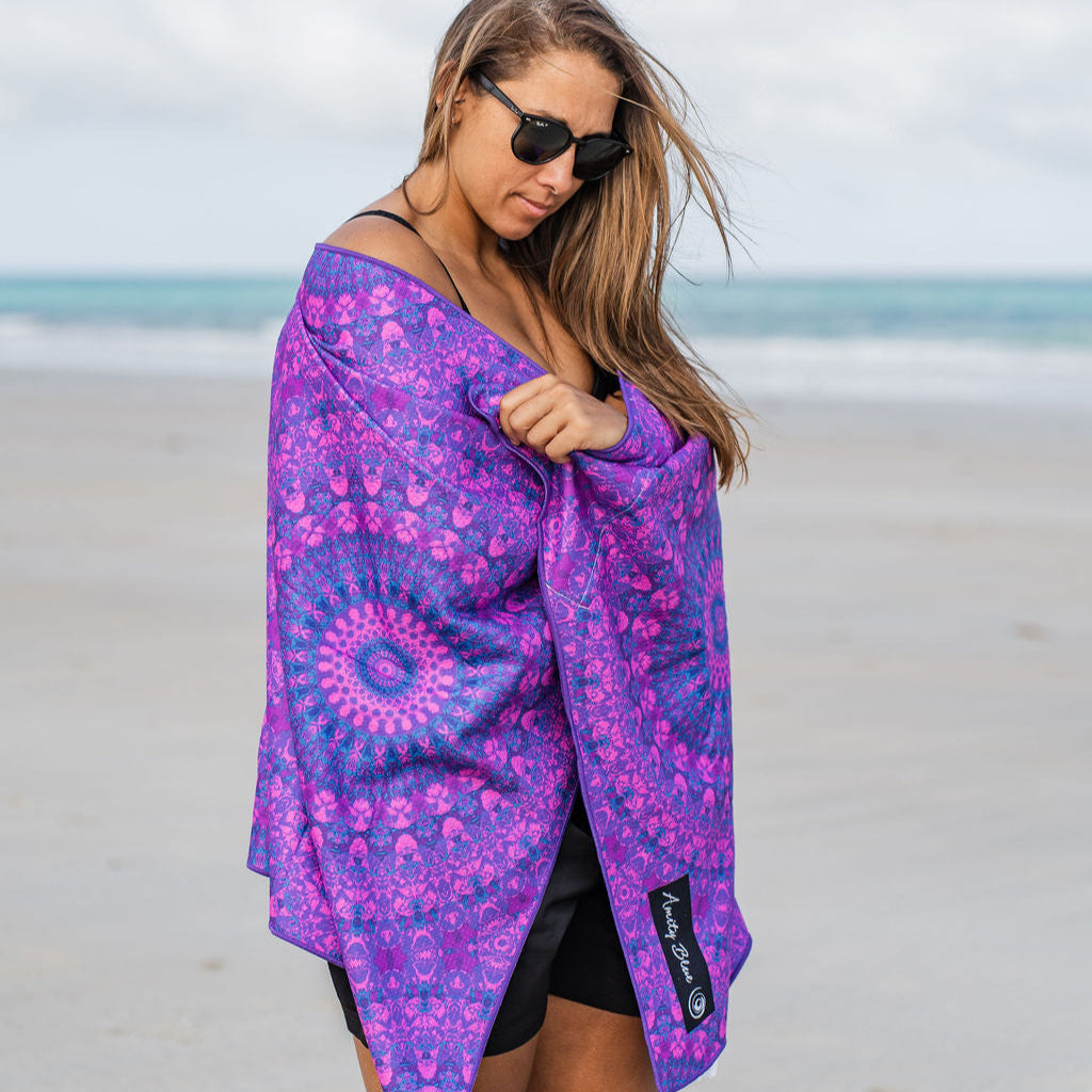 Woman on a beach with a purple sand free beach towel wrapped around her.
