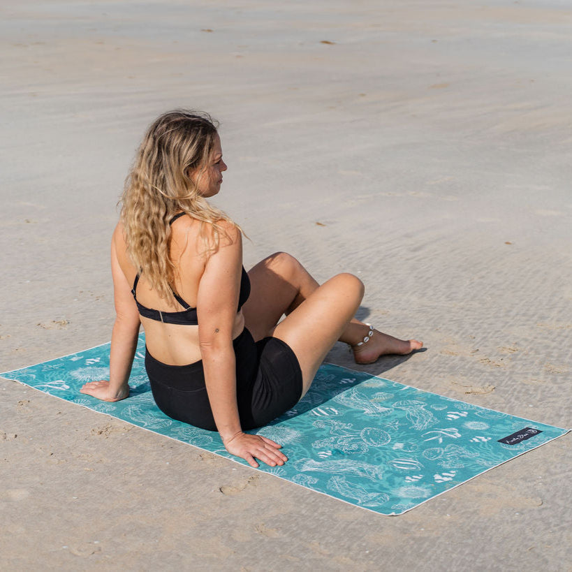 Woman sitting on a blue beach towel with a sea creature pattern on a sandy beach