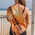 Person holding a gym towel with a Broome sunset design on it at the beach. Amity Blue logo written on the towel.