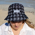 Lady wearing a black and white bucket hat made by Amity Blue using recycled plastic bottles. The beach is in the background.
