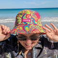 Lady wearing a muti-coloured bucket hat made by Amity Blue using recycled plastic bottles. The beach is in the background.
