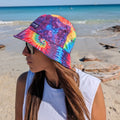 Lady wearing a muti-coloured tie-dye bucket hat made by Amity Blue using recycled plastic bottles. The beach is in the background.