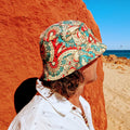 A person wearing a multicolored Amity Blue bucket hat, looking at the ocean.