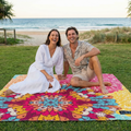 Couple sitting on a colorful mandala-patterned beach blanket at the beach.