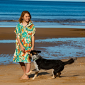 Woman in a colorful amity blue hooded towel, standing on a beach with a dog.