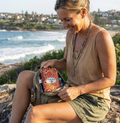 A Woman sitting by the ocean with a orange amity blue bag on her lap